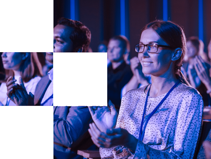 People sitting in an audience, clapping and wearing lanyards, with blue lighting in the background.